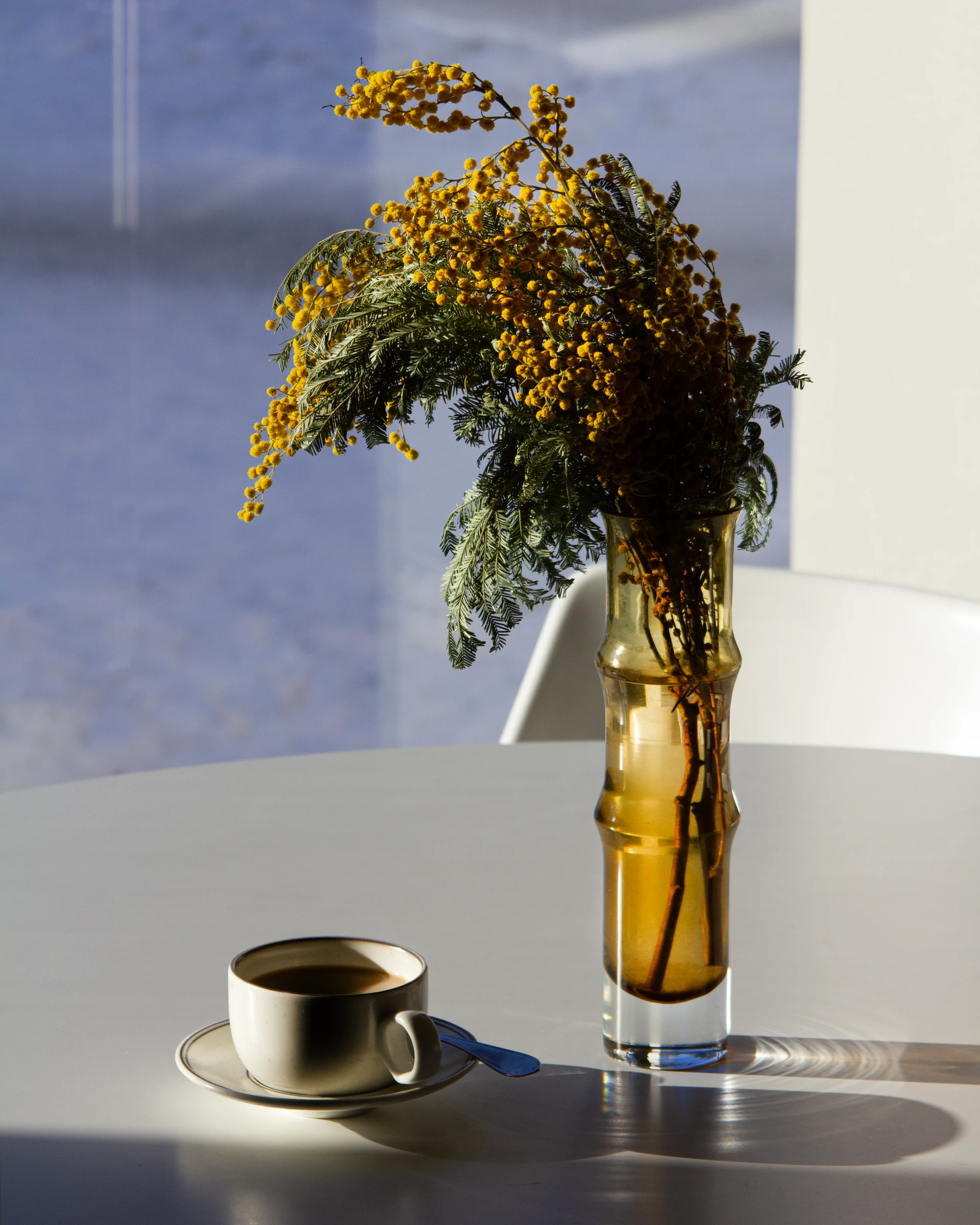 A coffee cup and yellow flowers on a sunny table at Nöösi